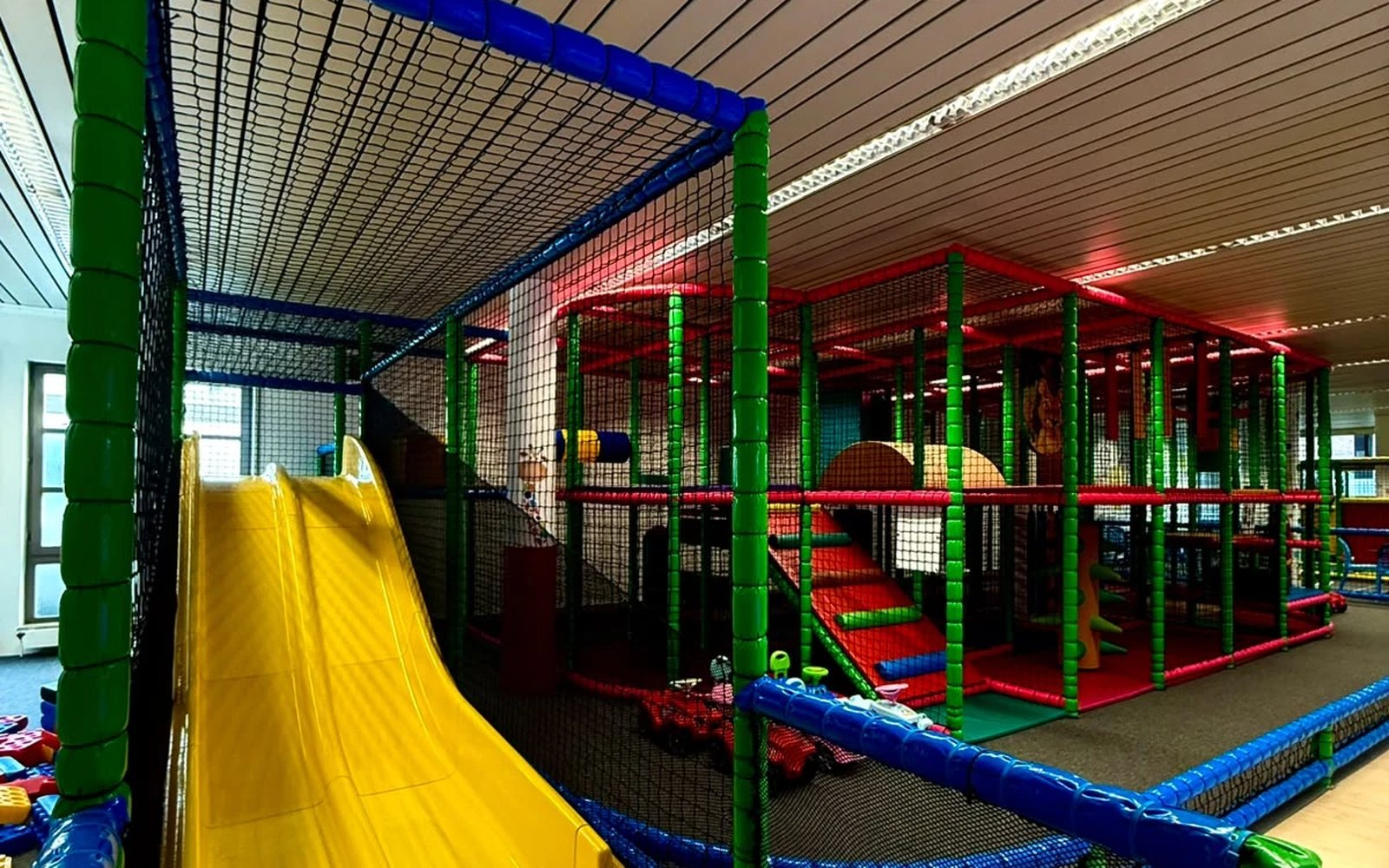 Die breite gelbe Rutsche im Spielbereich, dahinter das mehrstöckige Klettergerüst