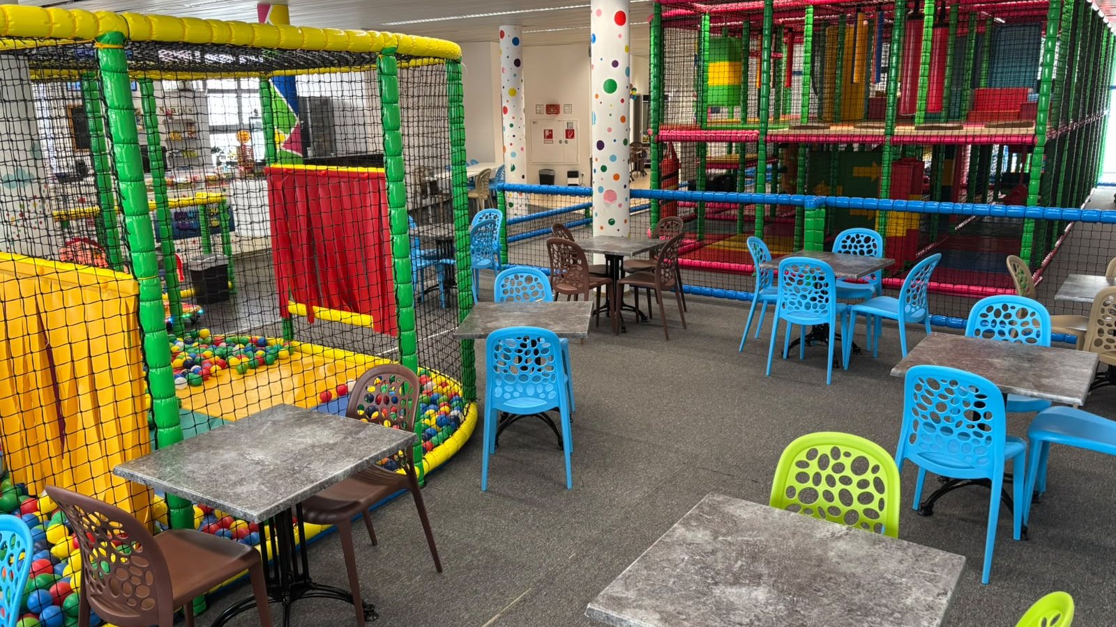 Blick über das Kinderspielcafé: Tische und Stühle im Elterncafé, dahinter Bällebad und Klettergerüst